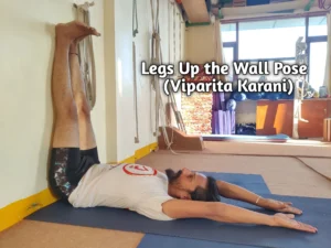 A person lying on their back with legs extended vertically against a wall in Legs Up the Wall Pose (Viparita Karani) yoga position