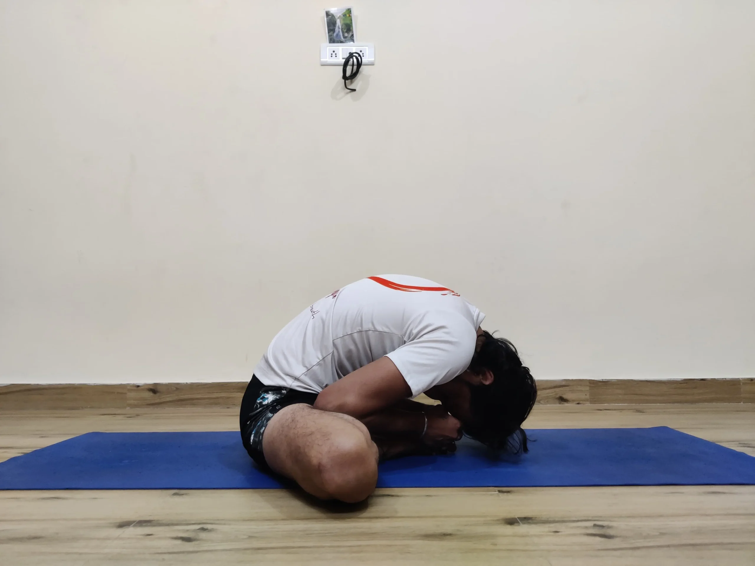 A person demonstrating Baddha Konasana B, or Bound Angle Pose variation, in yoga with the hands clasped around the feet.