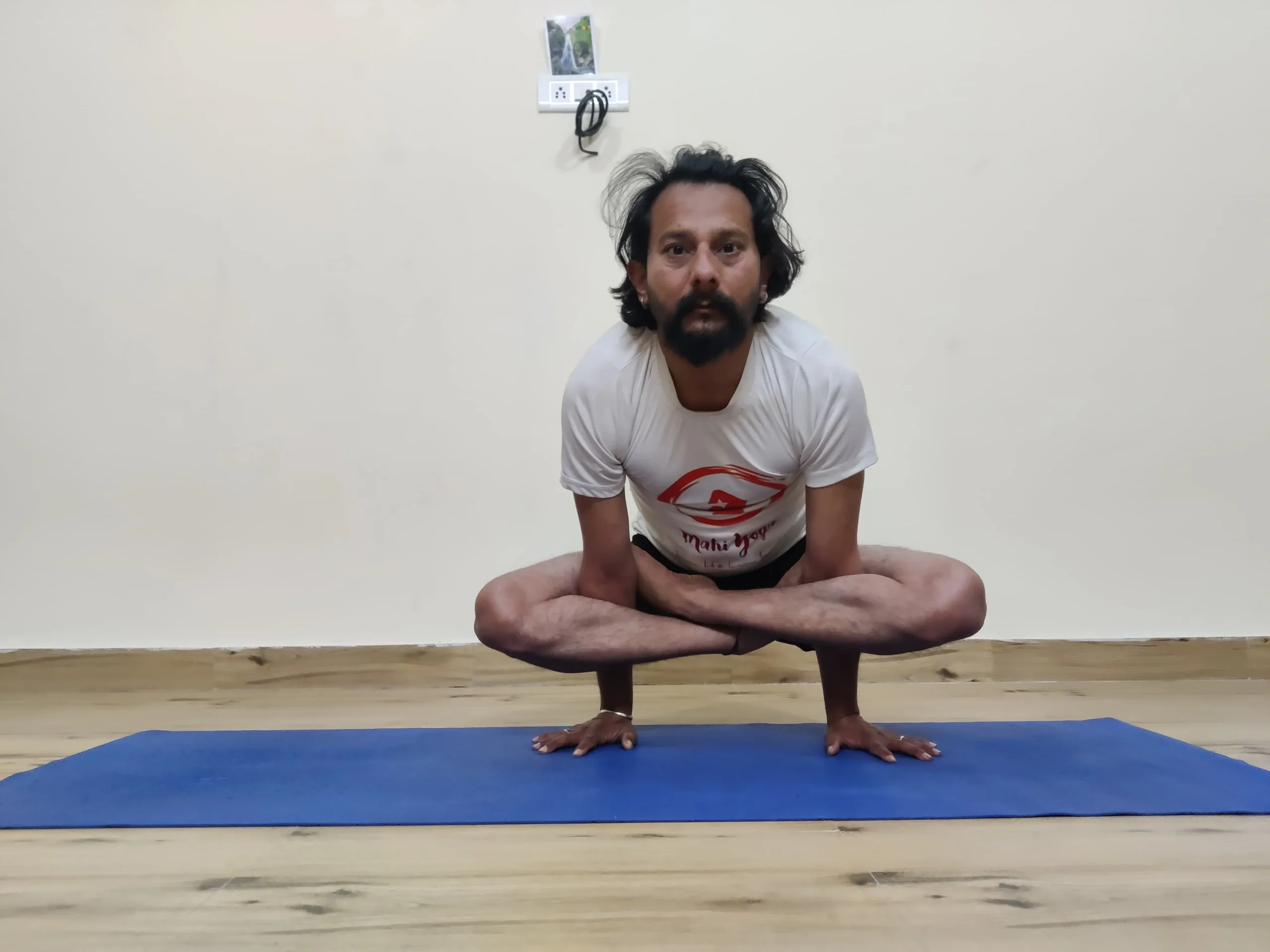 A person demonstrating Kukkutasana, also known as Rooster Posture, in yoga.