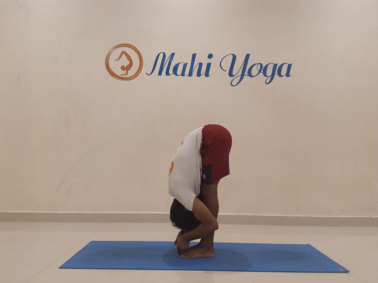 A man performing Padangusthasana, also known as Big Toe Posture, in a yoga studio.