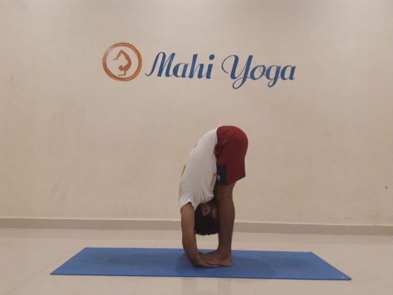 A man performing Padangusthasana, also known as Big Toe Posture, in a yoga studio.