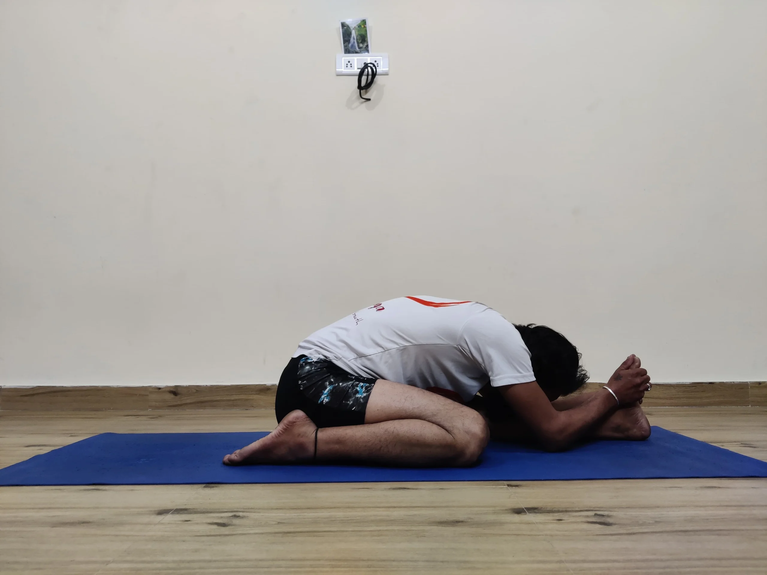 A person practicing Trianga Mukhaikapada Paschimottanasana, a seated yoga pose with one leg bent and the other leg stretched forward.