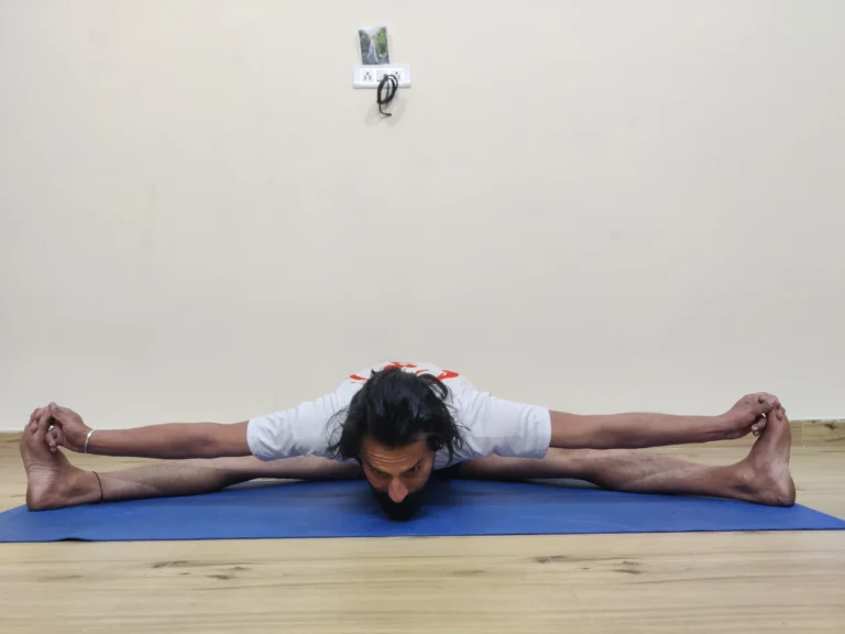 A man practicing Upavistha Konasana A, or Wide-Angle Seated Forward Bend, in yoga with legs spread apart.