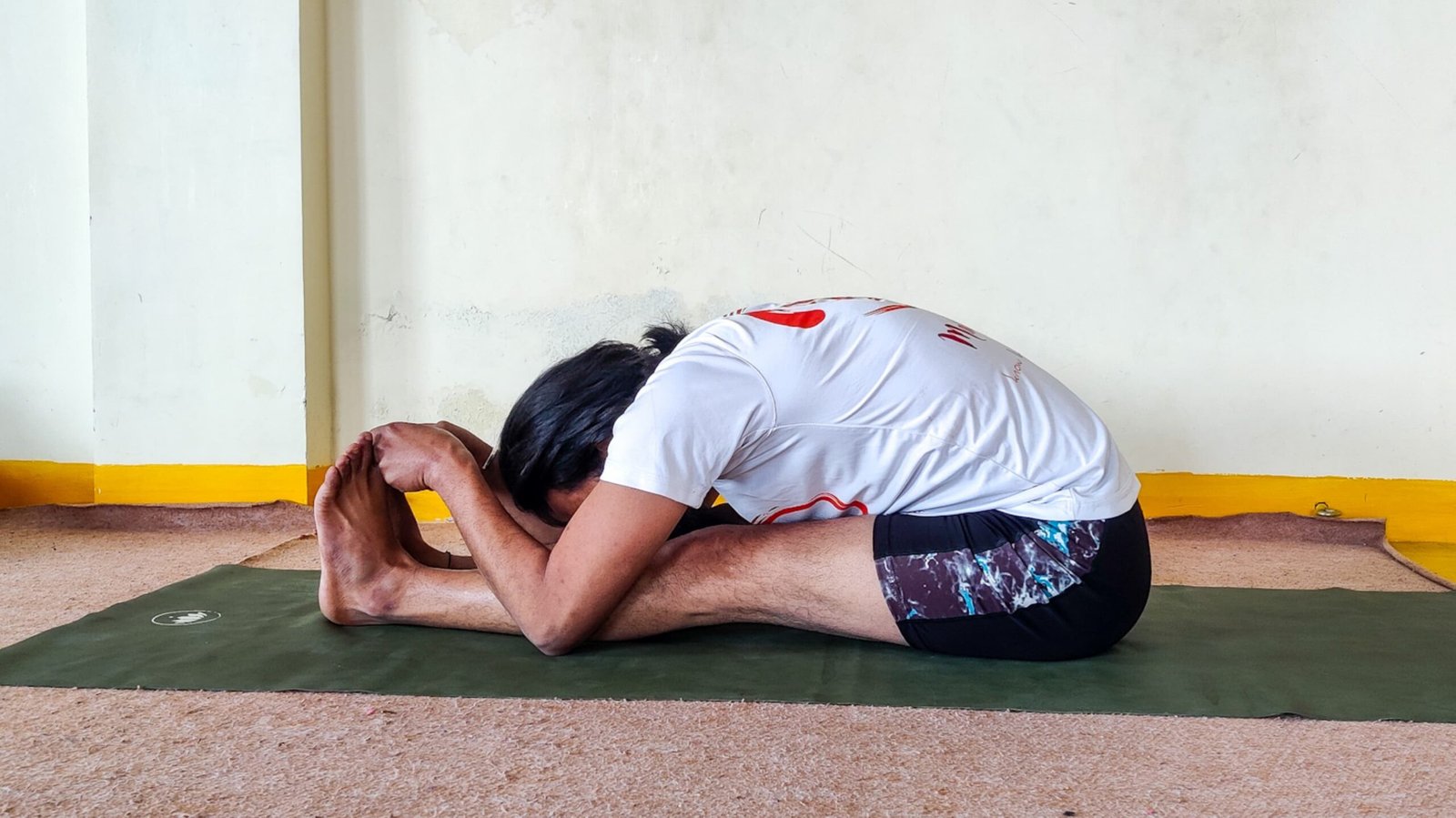 A man performing Paschimottanasana, also known as the Sitting Forward Bend yoga pose.