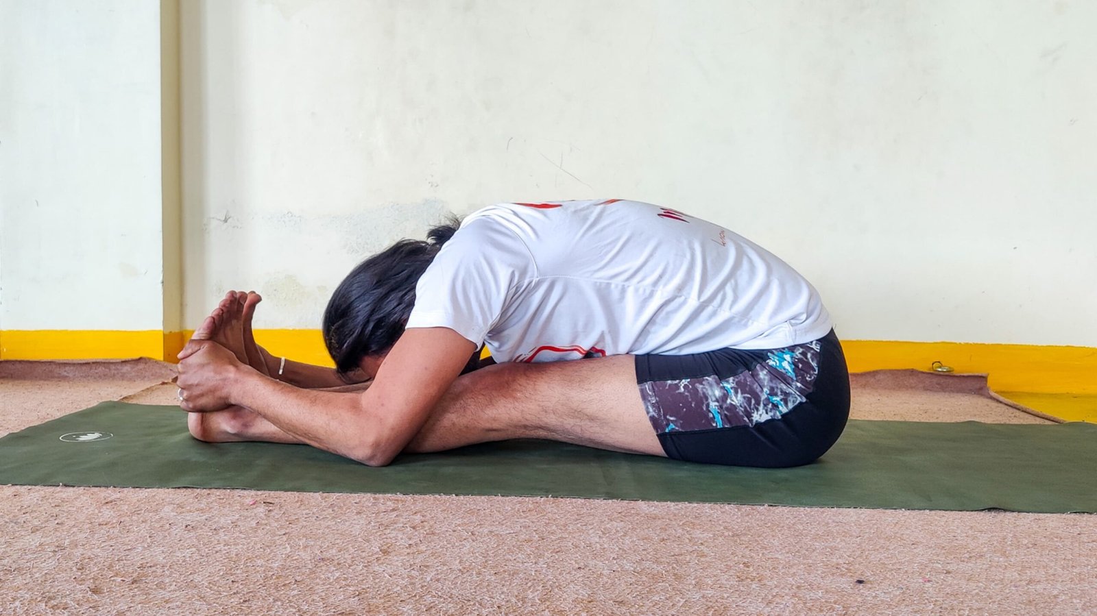 A man performing Paschimottanasana, also known as the Sitting Forward Bend yoga pose.