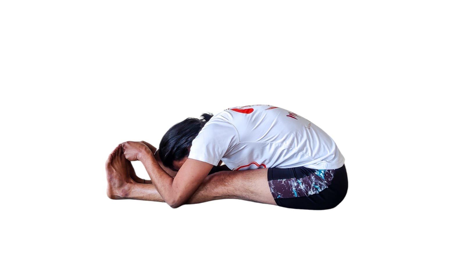 A man performing Paschimottanasana, a seated forward bend yoga pose, with legs extended and reaching towards the toes.