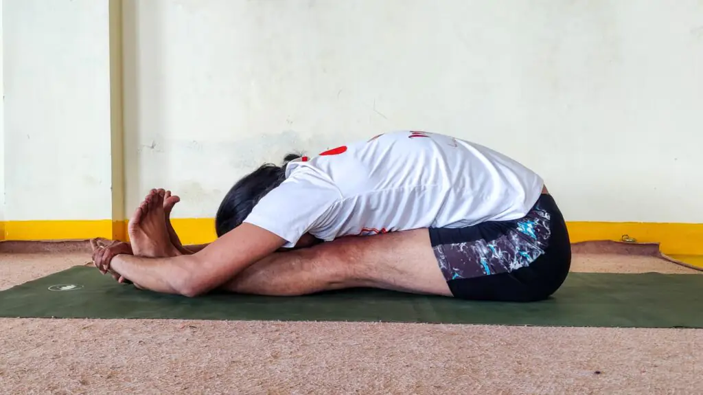 A man performing Paschimottanasana, also known as the Sitting Forward Bend yoga pose.